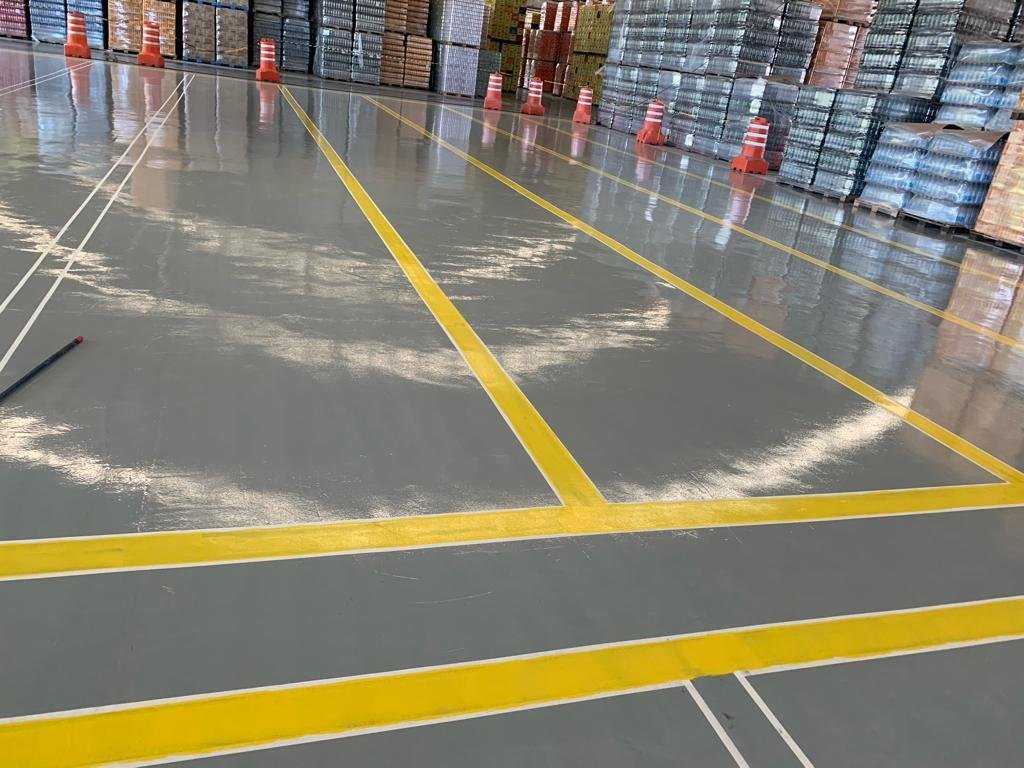 Piso industrial brilhante com faixas amarelas de demarcação em centro de distribuição