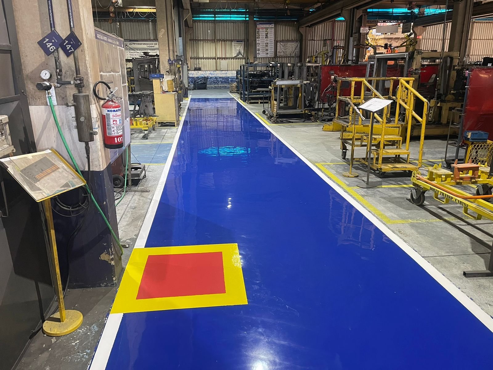 Piso epóxi industrial aplicado em estacionamento com faixa azul de circulação